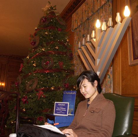 Graduate student Hye Kyeng Jeong studies by a giant menorah and a large Christmas tree on Wednesday in the North Lounge of the Illini Union. Thursday marks the third day of Hanukkah and the 16th day of shopping before Christmas. Online Poster
