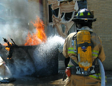 A Champaign firefighter puts out a trash bin fire on Saturday behind an apartment building on Healey Street in west Campustown. The fire broke windows and melted gratings on the building. No cause was known at the time of the fire and nobody was hurt. Che Online Poster
