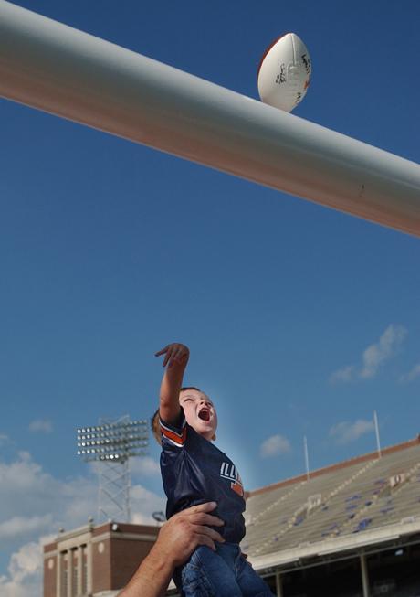 University employee Grant Nohren (not pictured) holds his son Logan, 2, up as he throws his newly-autographed football over the south field goal in Memorial Stadium Sunday at Fan Appreciation Day. E.B Halsey, Morris Virgil and head coach Ron Zook signed Online Poster
