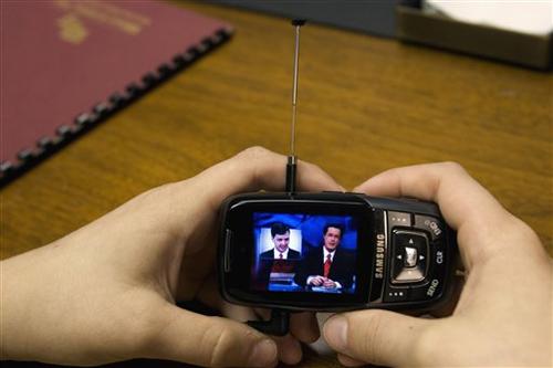 Brian Durham, 13, watches the Colbert Report on his cell phone, Wednesday, March 21, 2007 while his father, Charles Durham, vice president of Auto-Chlor Systems, not pictured, works in his office in Jacksonville, Fla. The Associated Press
