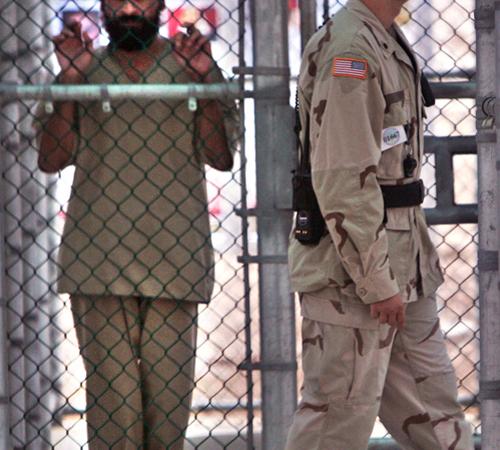 A Guantanamo detainee, complete facial identification not permitted, holds onto a fence as a U.S. military guard walks past, within the grounds of Camp 5 maximum security facility, Guantanamo Bay U.S. Naval Base, Cuba in this June 26, 2006 file photo. A S The Associated Press
