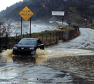 Jon Livingston splashes through the flooded intersection at North Coltrane Avenue at the entrance to the Oak Tree Gun Club in Newhall, Calif. Livingston and his two friends spent the afternoon pistol shooting at the club. Oak Tree used a tractor and shove Will Davison, The Associated Press
