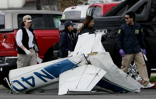 Investigators walk by the tail section of an airplane in the Corona Chevrolet dealership parking lot. Two planes collided in midair near the Corona Municipal Airport in Corona, Calif., killing five people Monday. Mark Zaleski, The Associated Press
