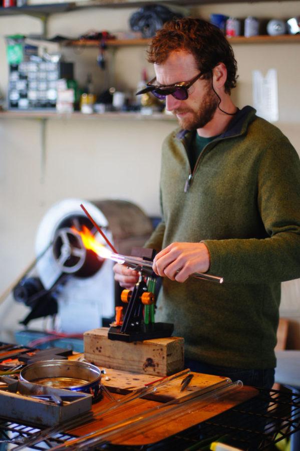 Jason Mack uses a blow torch to mold a pendant out of glass rods in his workshop in Champaign on Monday. He will be holding classes teaching glass blowing in April and May. 