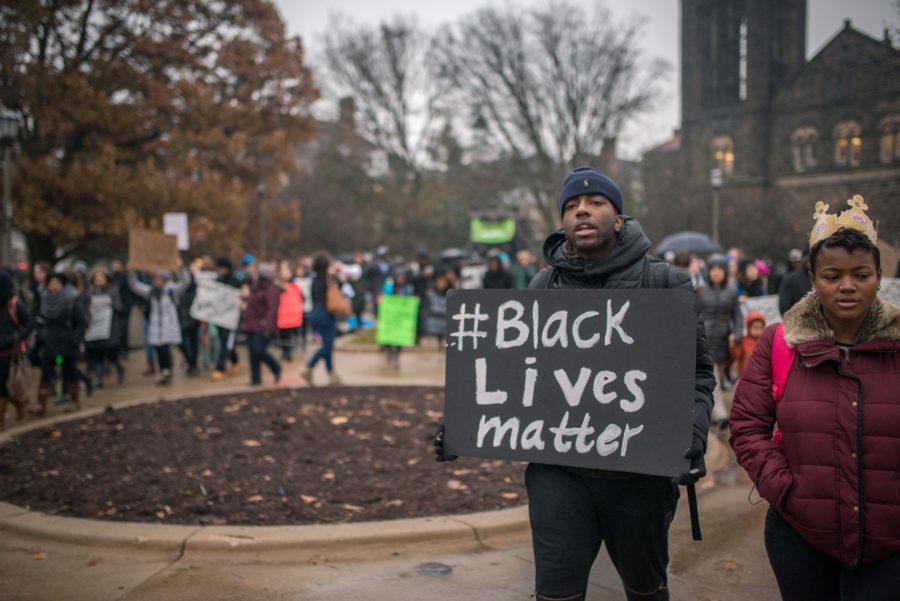 Students carry posters with messages in protest of police brutality in front of the Alma Mater statue on Monday, December 8, 2014.