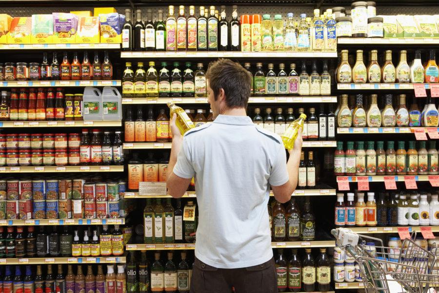 Young man in supermarket compares bottles of oil. Shopping intentionally can keep your pantry, and your life, organized.