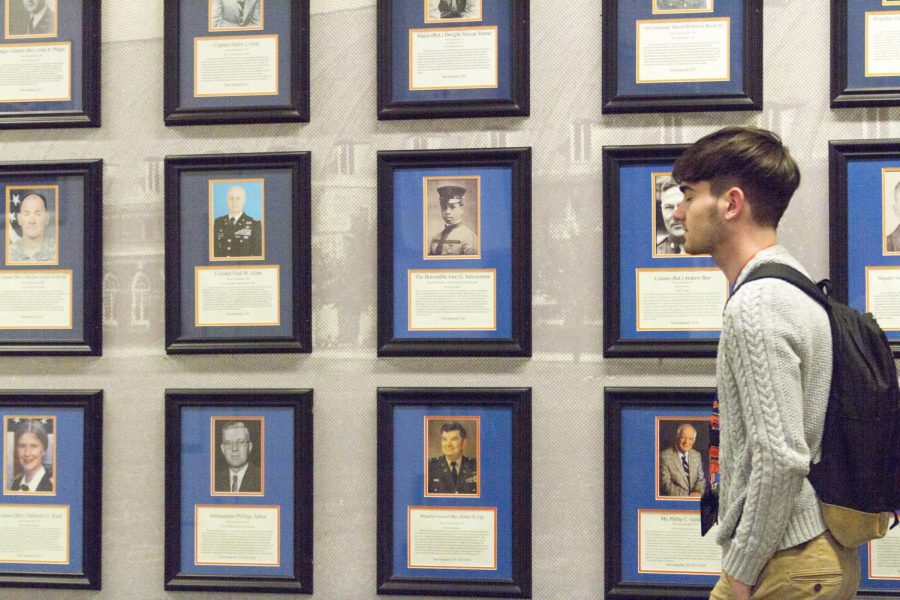 Student Colin Hec walks past photos of veterans on wall in Armory. Two University studies aim to explain mental health stigma.