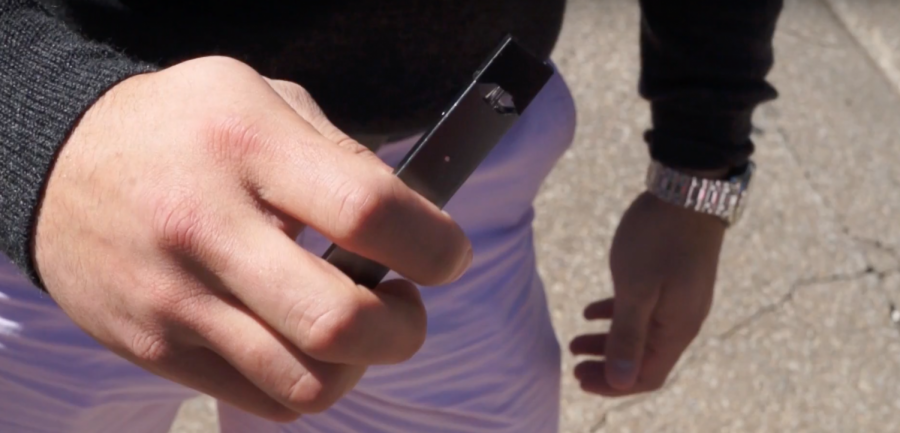 Student holding a Juul e-cigarette while walking to class on the Quad. Juuls contains nicotine salt from the same tobacco leaves found in cigarettes.
