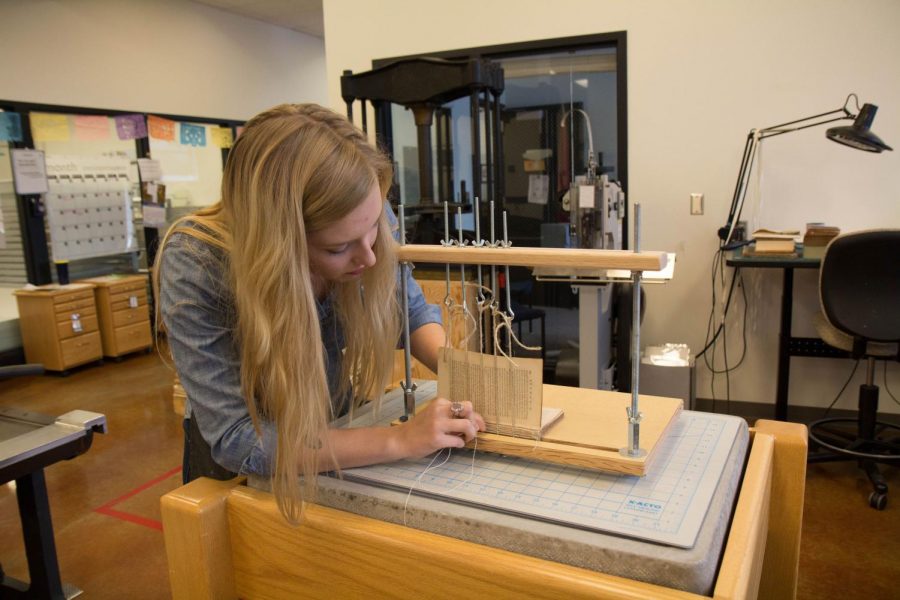 Anneka Vetter rebinds an old book before its eventual encasement in Fresh Press Studio’s case paper at the Oak Street Library on Friday. The studio is working to create sustainable paper. 
