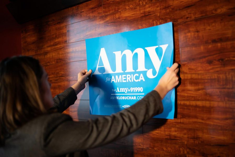 Staffer Greta Oanes tapes a Klobuchar sign on the wall, where Amy Klobuchar would speak to the Marion County Democrats, at a soup luncheon on Sunday, February 17, 2019 at Peace Tree Brewing Company in Knoxville, Iowa.