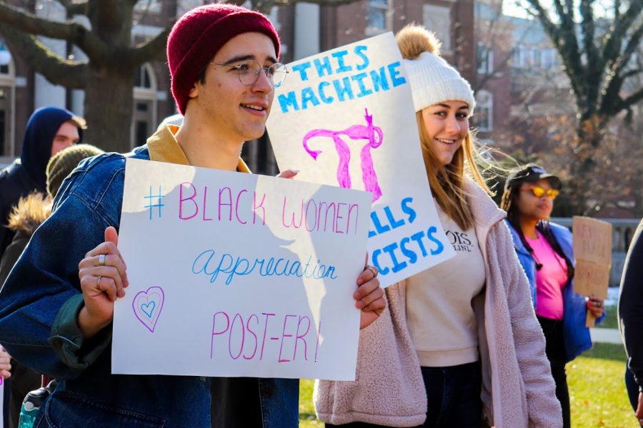 Two students hold up signs walking on the Main Quad for the Womens March.