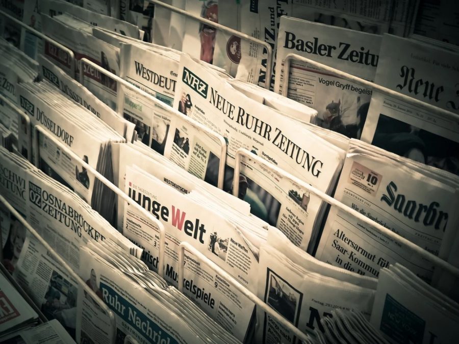 An assortment of newspapers rest on a tiered rack.