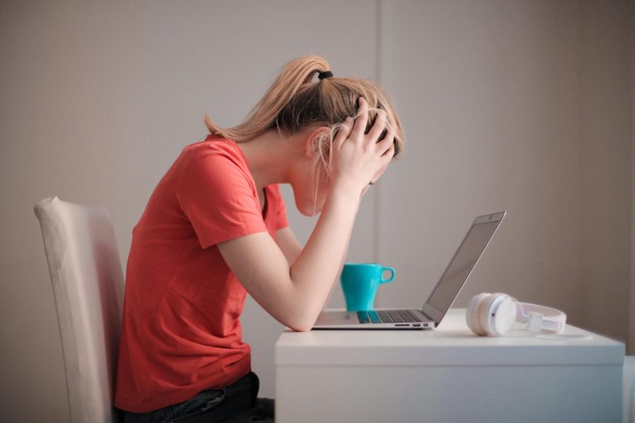 A woman holds her head in her hands as she stares at her laptop.