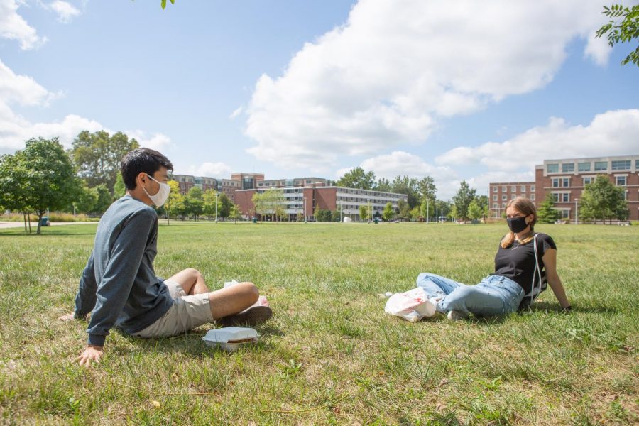 A pair of students wearing masks sit in the grass in the middle of the Ikenberry Commons on Sunday. Since the semester looks much different than in years past, students are adapting to life during a pandemic.