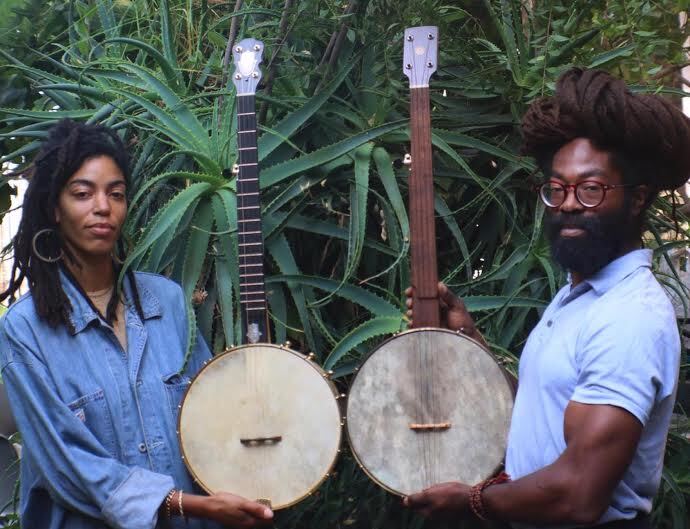 Hannah Mayree and Seymour Love of the Black Banjo Reclamation Project pose with their banjos in front of some foliage.