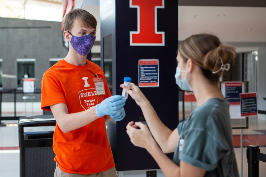 A University coronavirus testing site worker hands junior Jessica Wynveen a test tube at the State Farm Center testing site on Oct. 9. While Illinois is experiencing a rise in positivity rate, Champaign County has seen a steady rate, with UI depressing the region’s positivity.