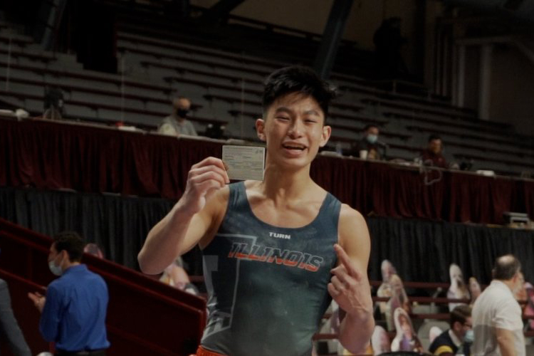 Sophomore Evan Manivong  sticks his landing and celebrates after by showing off his vaccine card during the meet against Minnesota on March 22. While originally meant as a joke between teammates, Manivong used the stunt to raise awareness about vaccinations.