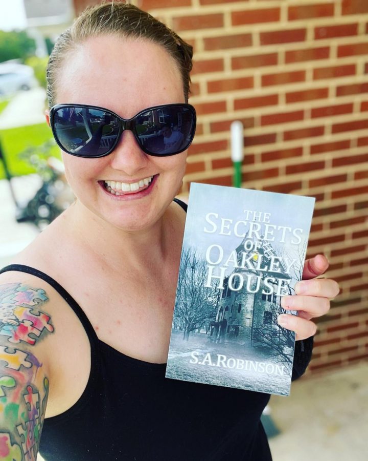 Author Sarah Robinson holds up her new novel The Secrets of Oakley House for a photo. Robinson is a Champaign native who was inspired by the victorian home and their stories in the area to write her first book.