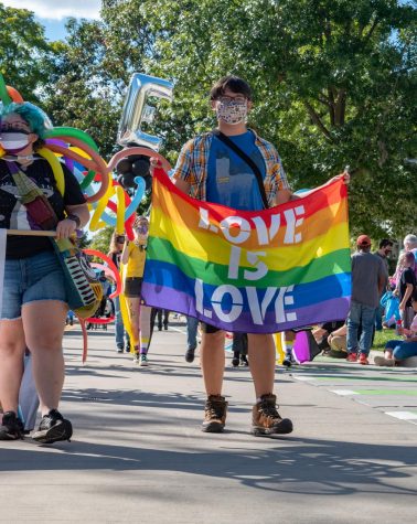 A person holds a LOVE IS LOVE flag while walking the CU Pride Parade route at CU Pride Fest, 2021.