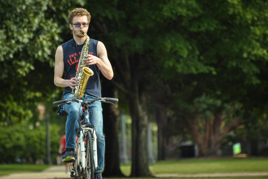Ian Copple, a senior in LAS, rides his bike on the Main Quad playing the saxophone which he refers to as saxo-biking.
