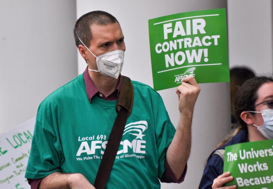 Joshua Hollingsead holds a sign, Fair contract now, during the protest outside of the Illini Union on Wednesday. The protest was organized by AFSCME Local 3700 demanding back pay and wage increase from the University. 
