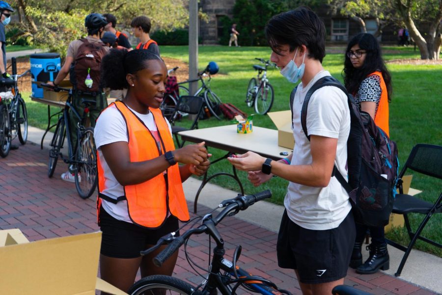 Volunteer Jada Allen (left), junior in LAS, hands Nicholas Costello, freshman in Engineering, a bike light during the Light the Night bike event on Thursday. 