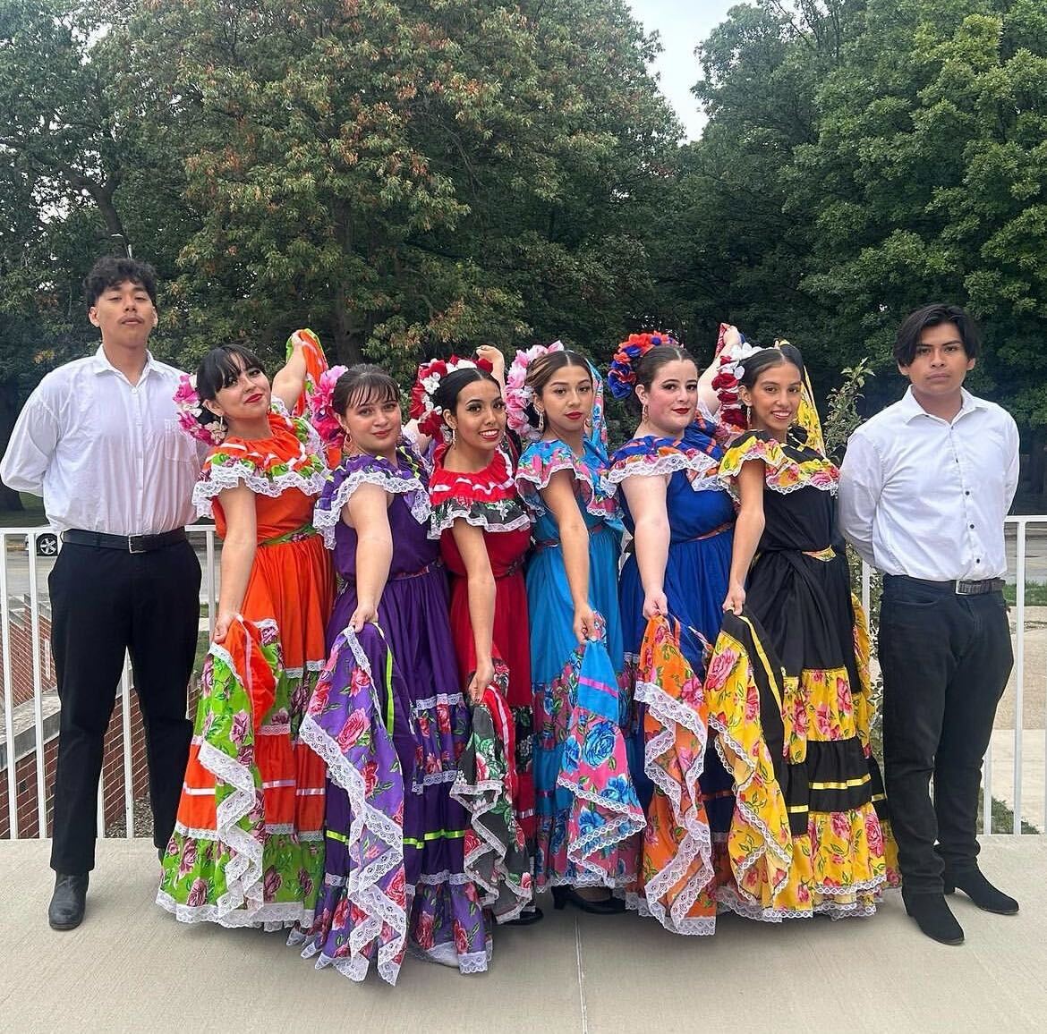 Ballet Folklorico dancers stand outside alongside each other in traditional Jalisco dresses and charro-style white shirts.