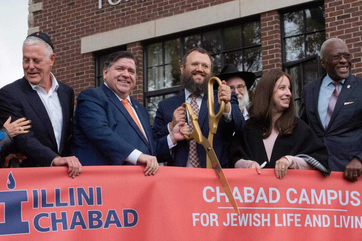 Governor+JB+Pritzker+and+Rabbi+David+Tiechtel+share+the+scissors+at+the+ribbon+cutting+of+the+Illini+Chabad+grand+opening+on+Thursday.+The+two+smile+for+the+photographers+as+the+audience+counts+down+from+ten.%0A