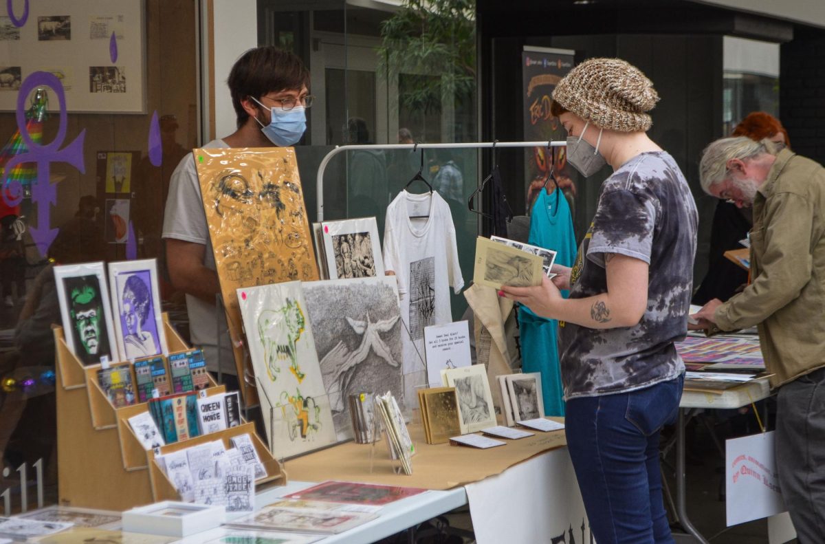Urbanas Small Press Festival is set up in Lincoln Square mall for artists to sell and show off their work on Oct. 28. Artist talks to a potential customer as the customer looks through their work.