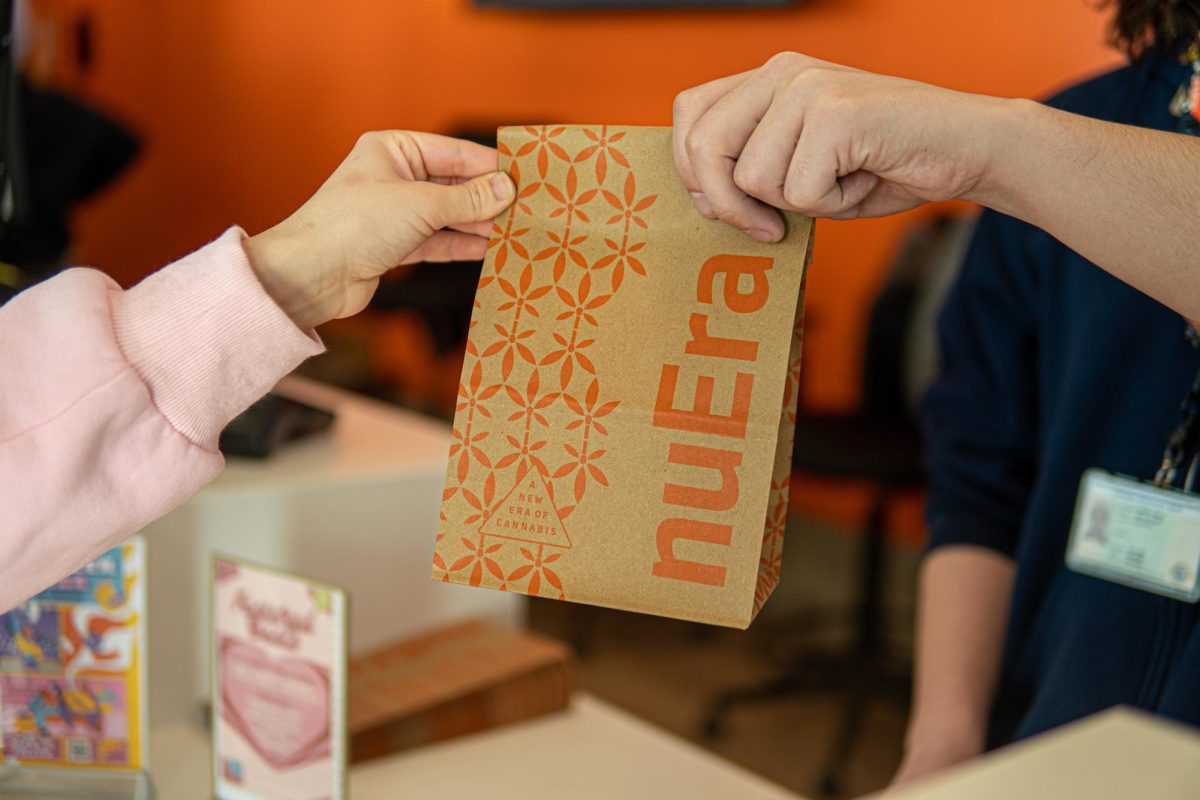 A customer grabs a branded nuEra bag from the employee at the counter. nuEra, located at the corner of Green and First streets, serves as a haven for all high-llini, as their billboard says.