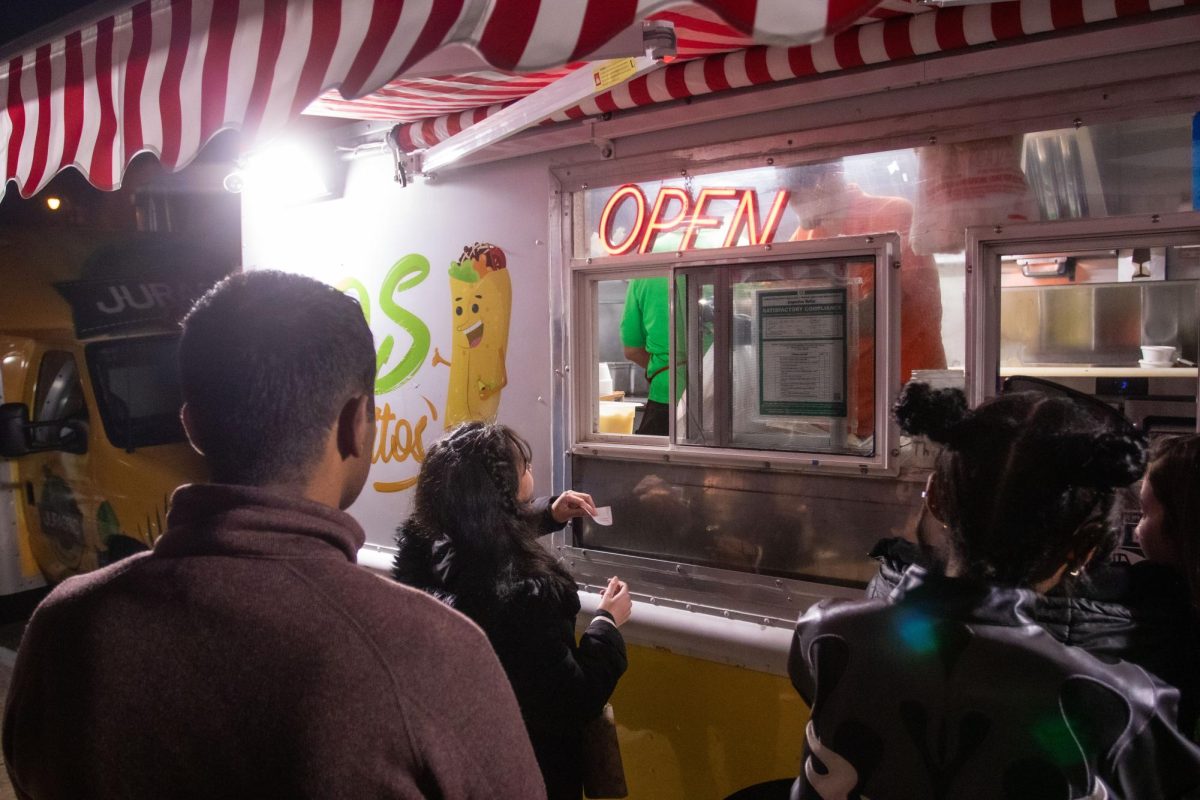 Customers line up to recieve their orders from the Mo’s Burritos food truck parked at Fifth and Green Streets at night on March 2.