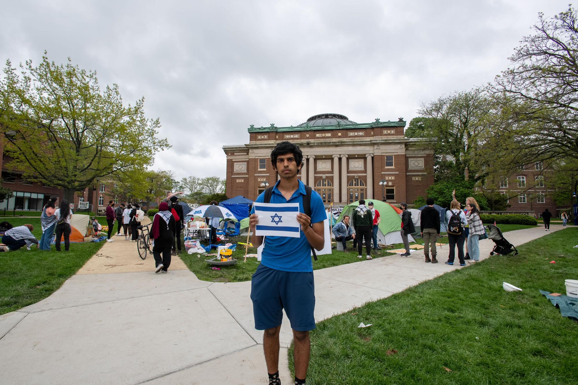 A student, Sean, who requested to be identified by first name only, stands with a printed photo of a flag of Israel in front of the encampment.