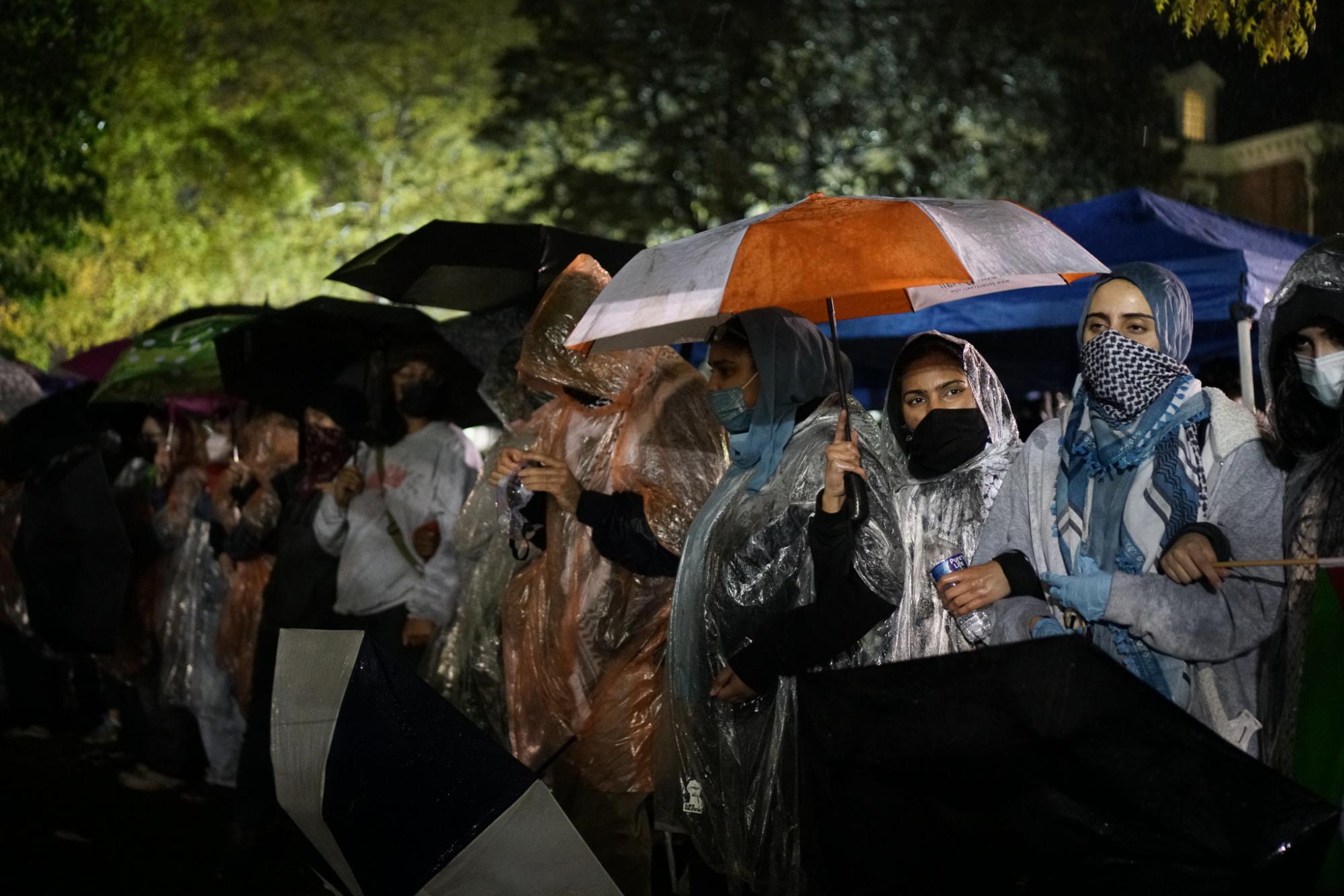 Protesters stand huddled under umbrellas on Friday night.