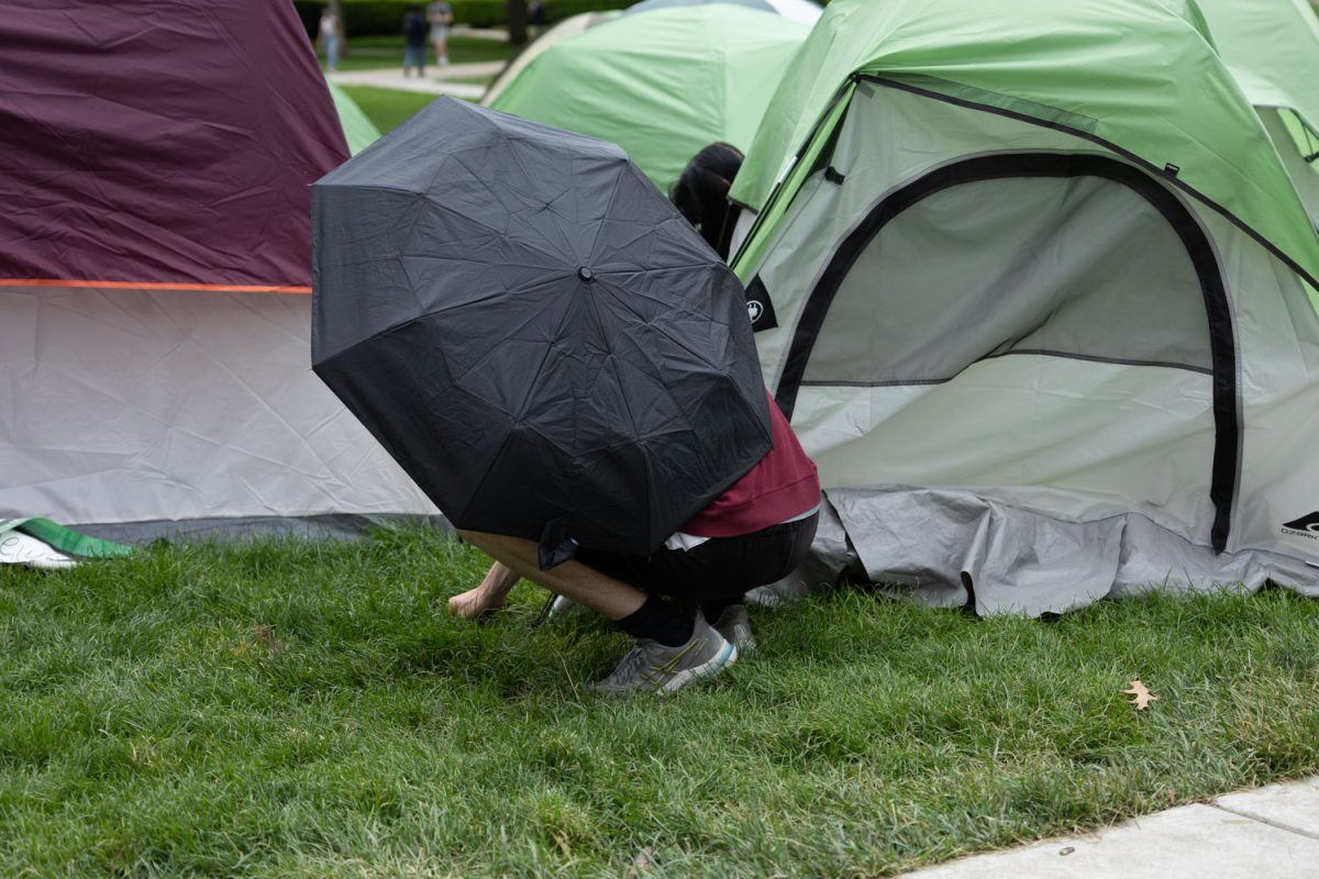 A protestor secures a tent to the ground after harsh winds dismantles tents on Tuesday morning.