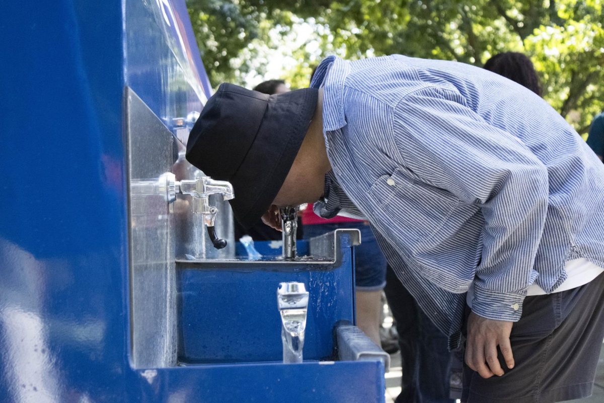 A Quad Day attendee drinks from the water station on the Main Quad to stay hydrated in the extreme heat.