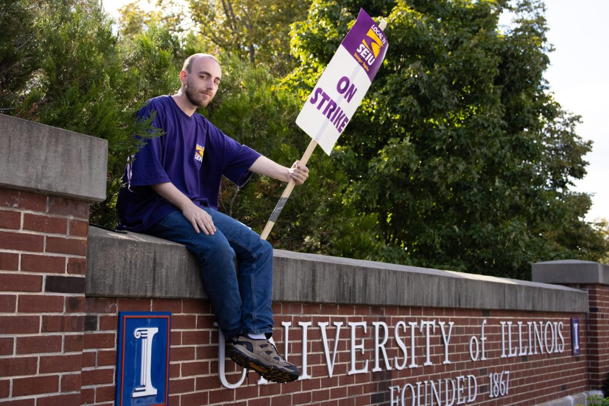 Dylan Cockrum, a building service worker at University Laboratory High School for six years, sits on a sign on the corner of Lincoln Avenue and Green Street outside ISR on Thursday, Sept. 26, 2024, the fourth day of the Service Employees International Union strike. 