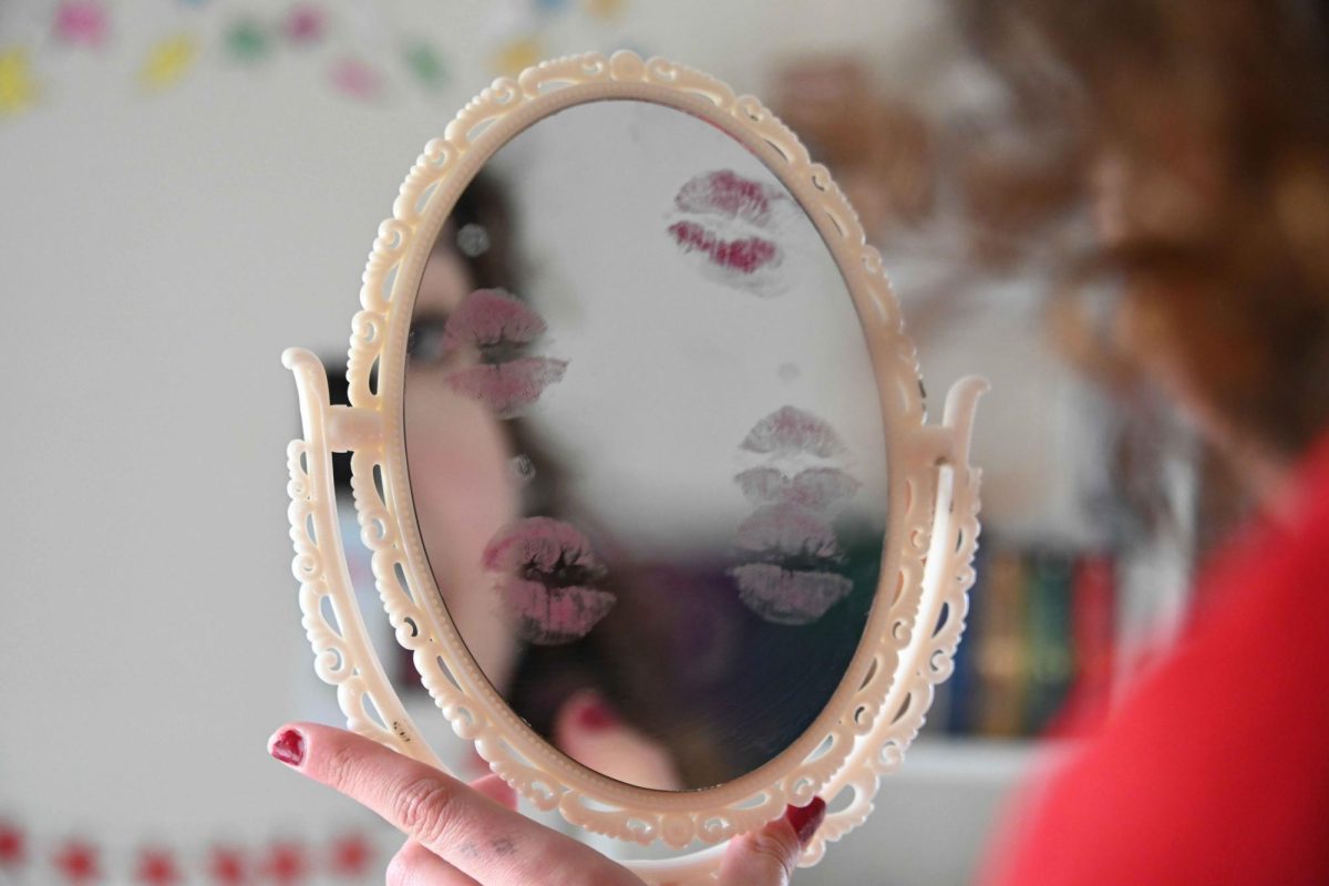 A woman gazes into a mirror covered in lipstick kiss marks as she gets ready for a date.