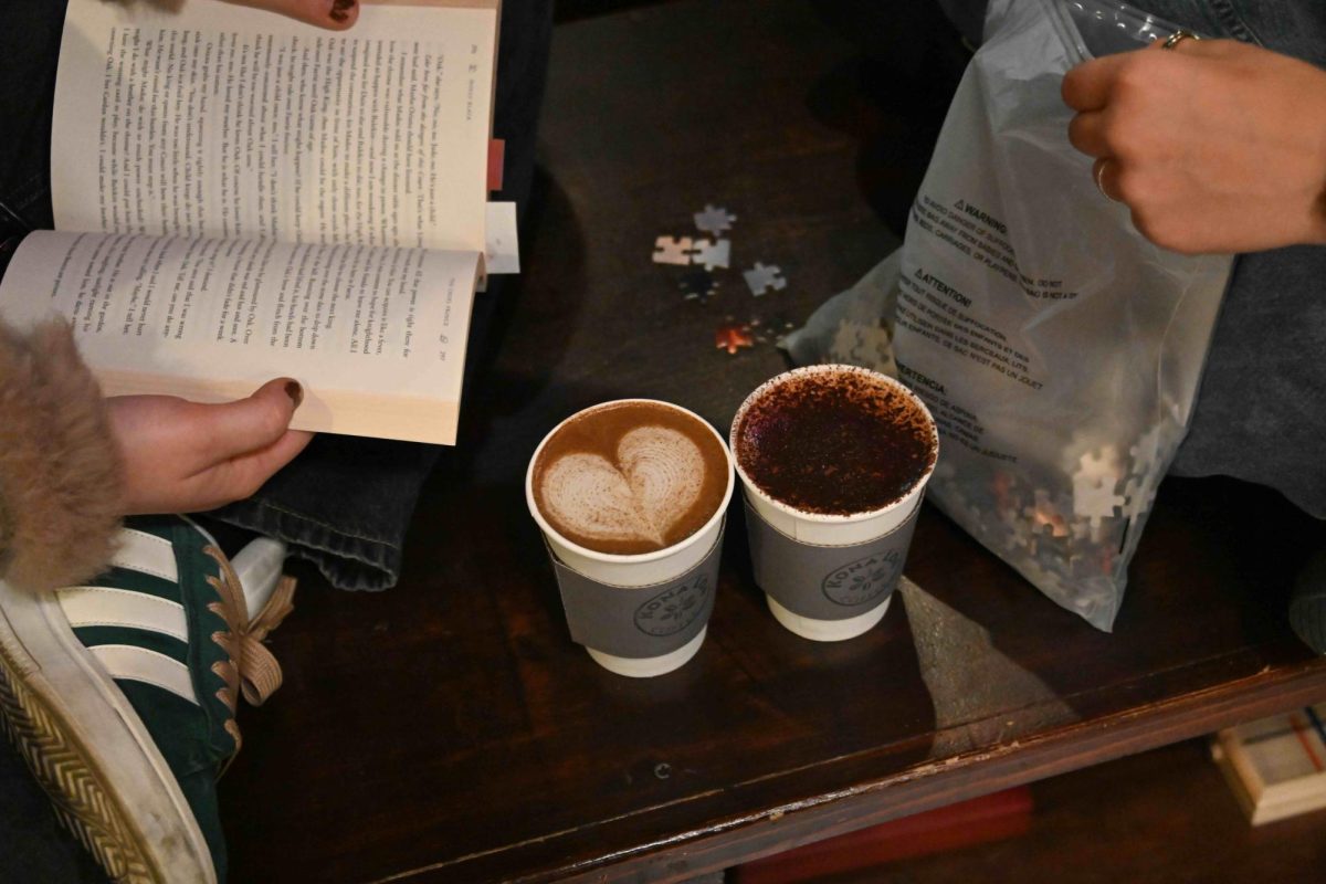 A couple shares coffees while they read and work on a puzzle.