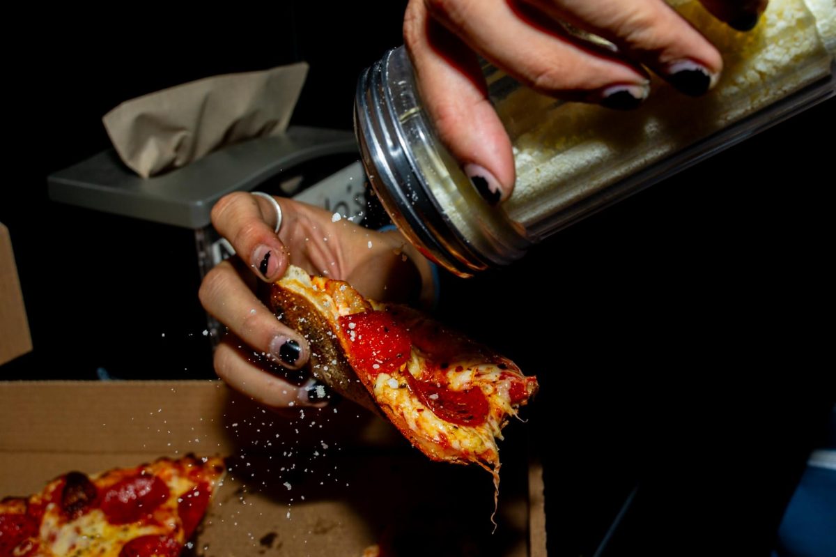 A student sprinkles parmesan over a pepperoni pizza at Manolo's on Feb. 10.