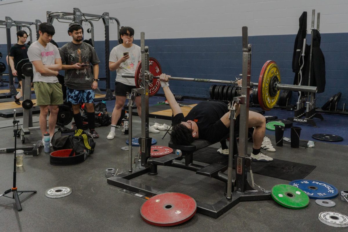 A group of people gather around someone bench pressing in the Activities and Recreation Center on Feb. 21.
