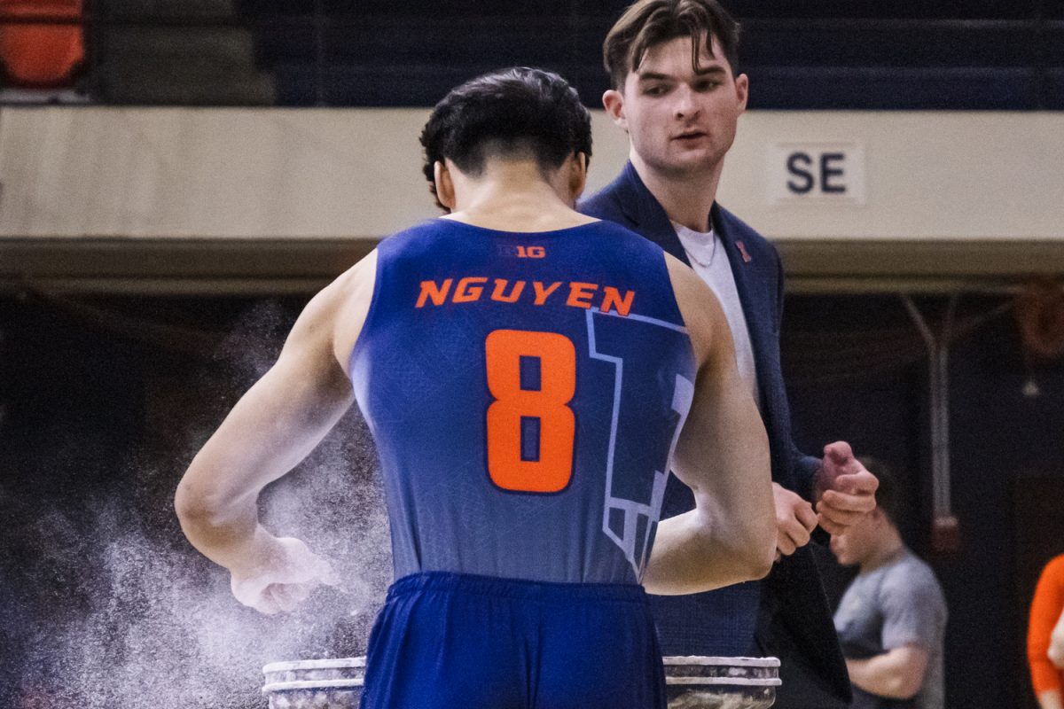 Assistant coach Connor McCool speaks to freshman Matthew Vu Nguyen before he competes on the parallel bars at a meet on March 1. Illinois won the meet against Army and Greenville with a final score of 316.700.