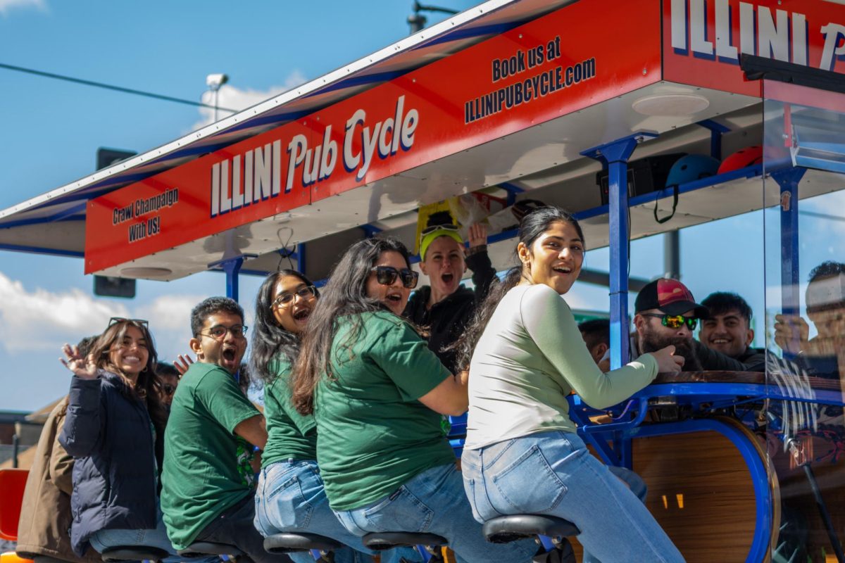 Illini Pub Cycle riders cheer as they ride down Green Street during Unofficial on Saturday afternoon.