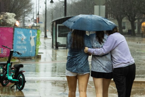 Three people huddle under an umbrella as they rush down Wright Street in the rain at 1:45 p.m. on March 30.
