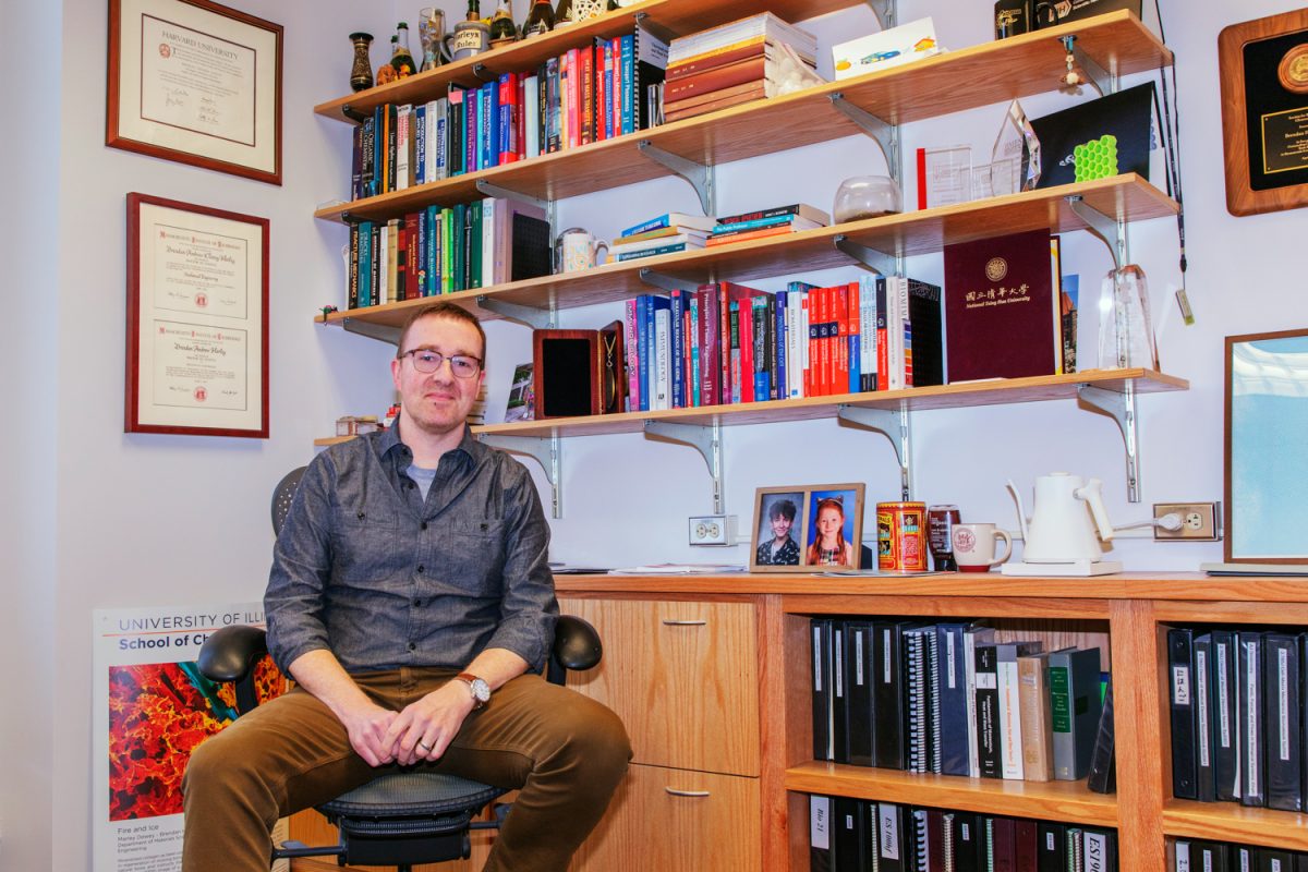 Brendan Harley in front of his shelf decorated with multiple books, awards and personal mementos in his Roger Adams Laboratory office on April 1. He proudly expresses that the shelves and desks in his office were made by University students.