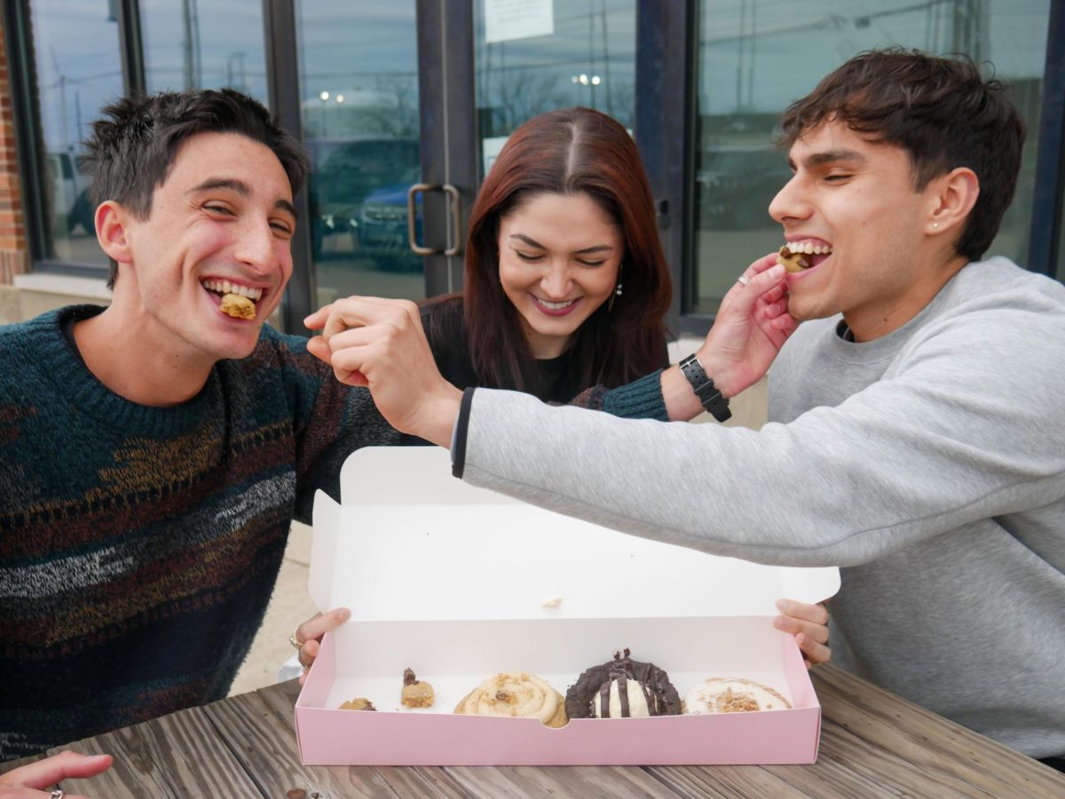 Sam Blaker (left), Iva Scekic (middle) and Paul Klapperich (right) make up the executive board of Crumbl Club. The trio sits and enjoys this weekʼs flavor selection outside of the Crumbl on Neil Street in Champaign on April 9.