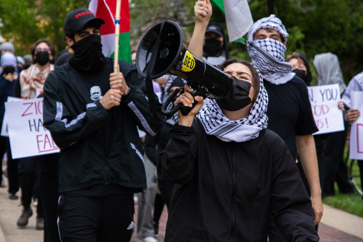 A speaker with a megaphone leads fellow demonstrators donning black clothing, masks and keffiyehs during a pro-Palestine march through the Main Quad on May 2. The protest began with a rally in front of Alma Mater before finishing with the march.