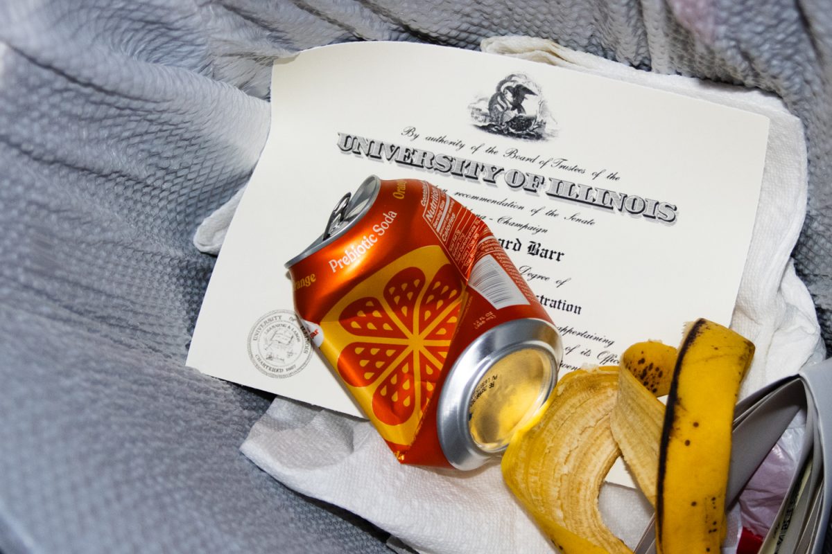 An Illinois diploma lies in a trash can surrounded by other various rubbish items.