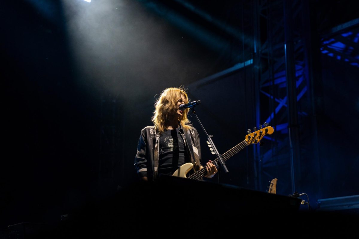 Jooyeon sings into the microphone and expertly plays his bass guitar.