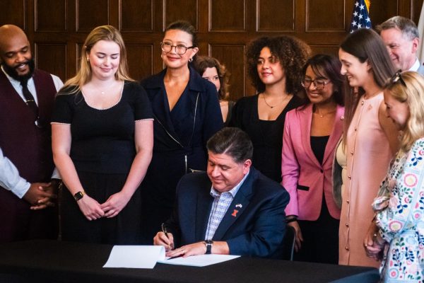 Illinois Governor JB Pritzker signs House Bill 3637 and House Bill 3709 at the University YMCA on Friday. He is surrounded by members of the Illinois General Assembly, Illinois senators and former members of the University's chapter of Planned Parenthood Generation Action.