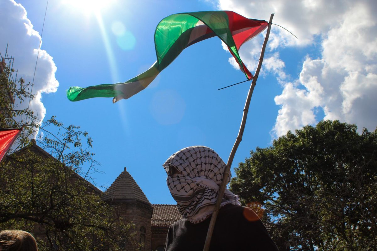 A protestor holds a Palestinian flag during a speech from an event organizer at Alma Mater Friday. The rally was in support of the Global Sumud Flotilla, an international civilian aid mission aiming to break Israel’s blockade of Gaza. 